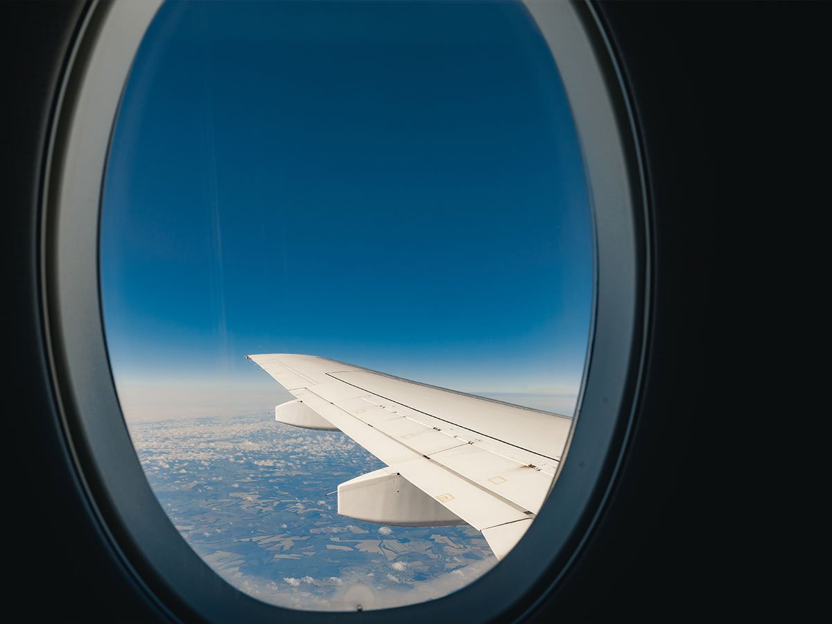 Vista da asa de uma aeronave pela janela oval da cabine, sobre nuvens